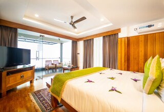 A hotel room with a bed, a television on a wooden cabinet, a ceiling fan, an air conditioning unit, and a view of the outdoors.