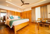 A bedroom with a wooden bed, a ceiling fan, a wooden table with chairs, and a large window with curtains.