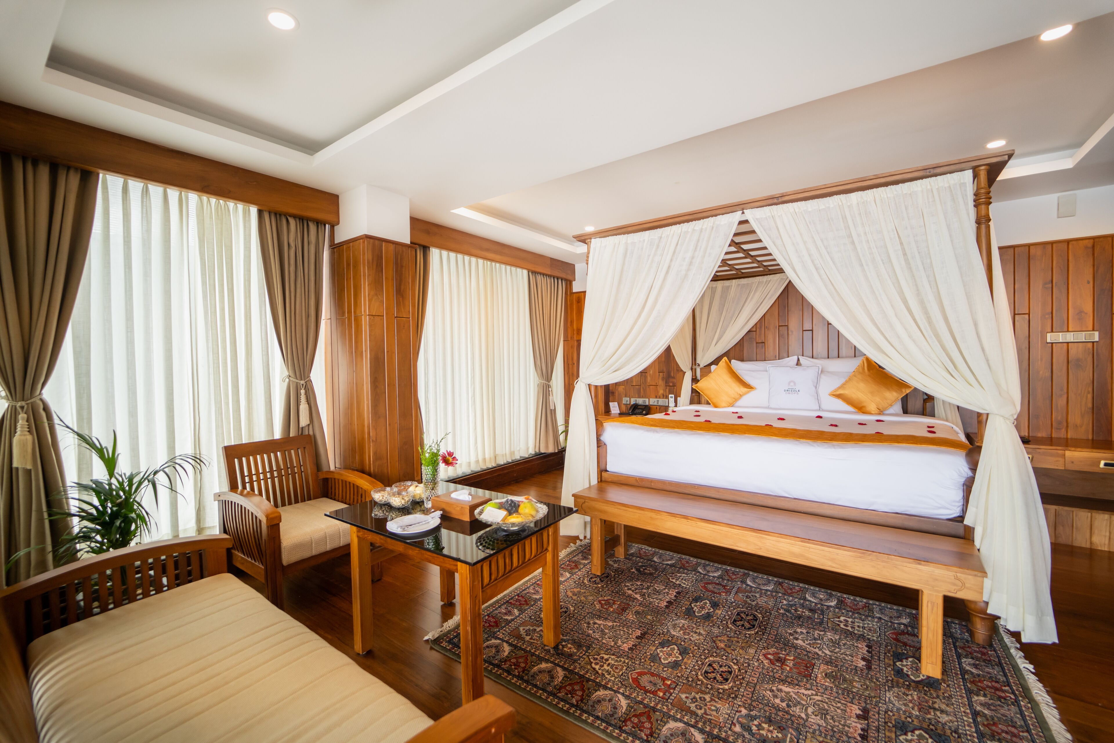 A four-poster bed with a canopy, a wooden desk with a chair, a small table with a vase, and a large window with curtains.