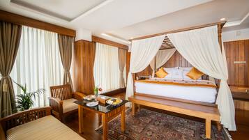 A four-poster bed with a canopy, a wooden desk with a chair, a small table with a vase, and a large window with curtains.