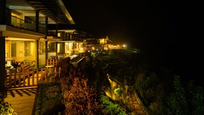 Un hotel moderno con varios pisos, asientos exteriores y vistas del paisaje circundante.