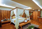 A spacious bedroom with a four-poster bed, wooden wardrobe, and a sitting area with a desk and chair.