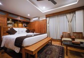 A bedroom with a wooden bed, a bench, a chair, a large rug, and a ceiling fan.