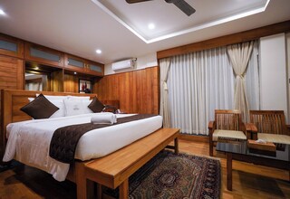 A bedroom with a wooden bed, a bench, a chair, a large rug, and a ceiling fan.