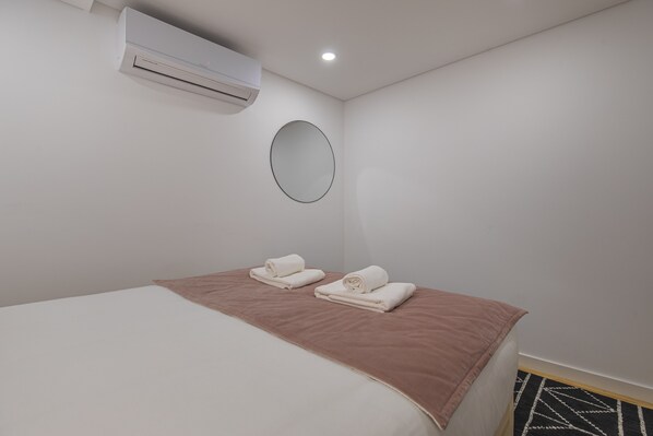 Une chambre d’hôtel avec un lit, deux serviettes, un miroir rond et un appareil de climatisation.