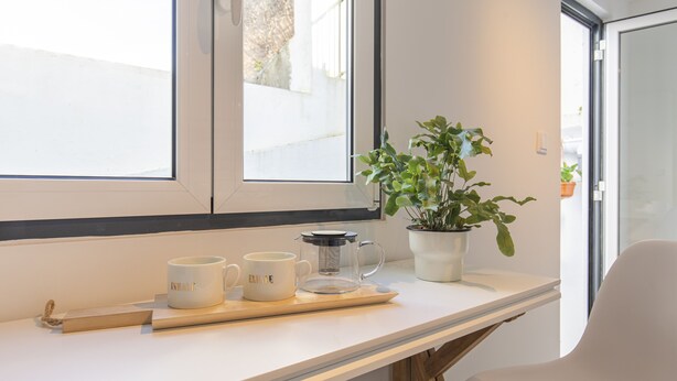 Une pièce moderne avec un bureau blanc, deux tasses blanches, une cafetière en verre et une plante en pot.