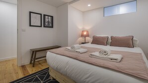 Une chambre moderne avec un lit en bois, du linge de lit blanc, un plaid rose et une lampe de chevet.