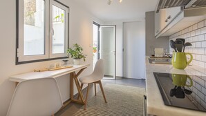 Une cuisine moderne avec un plan de travail blanc, une chaise en bois, une plante en pot et un pichet vert posé sur le plan de travail.