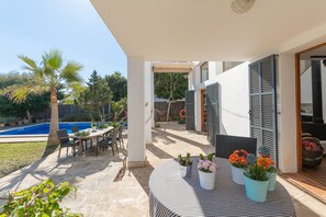 An outdoor patio area with a pool, dining table, chairs, and potted plants.