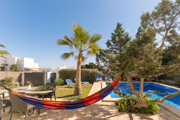 A poolside area with a hammock, lounge chairs, a palm tree, and a pool.