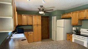 A kitchen with granite countertops, wooden cabinets, a white refrigerator, a stove, and a ceiling fan. - Gemme au paradis (Lake Worth)