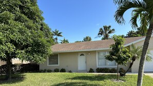 A single-story house with a beige exterior, a red-tiled roof, and a front yard with grass and a palm tree. - Gemme au paradis (Lake Worth)
