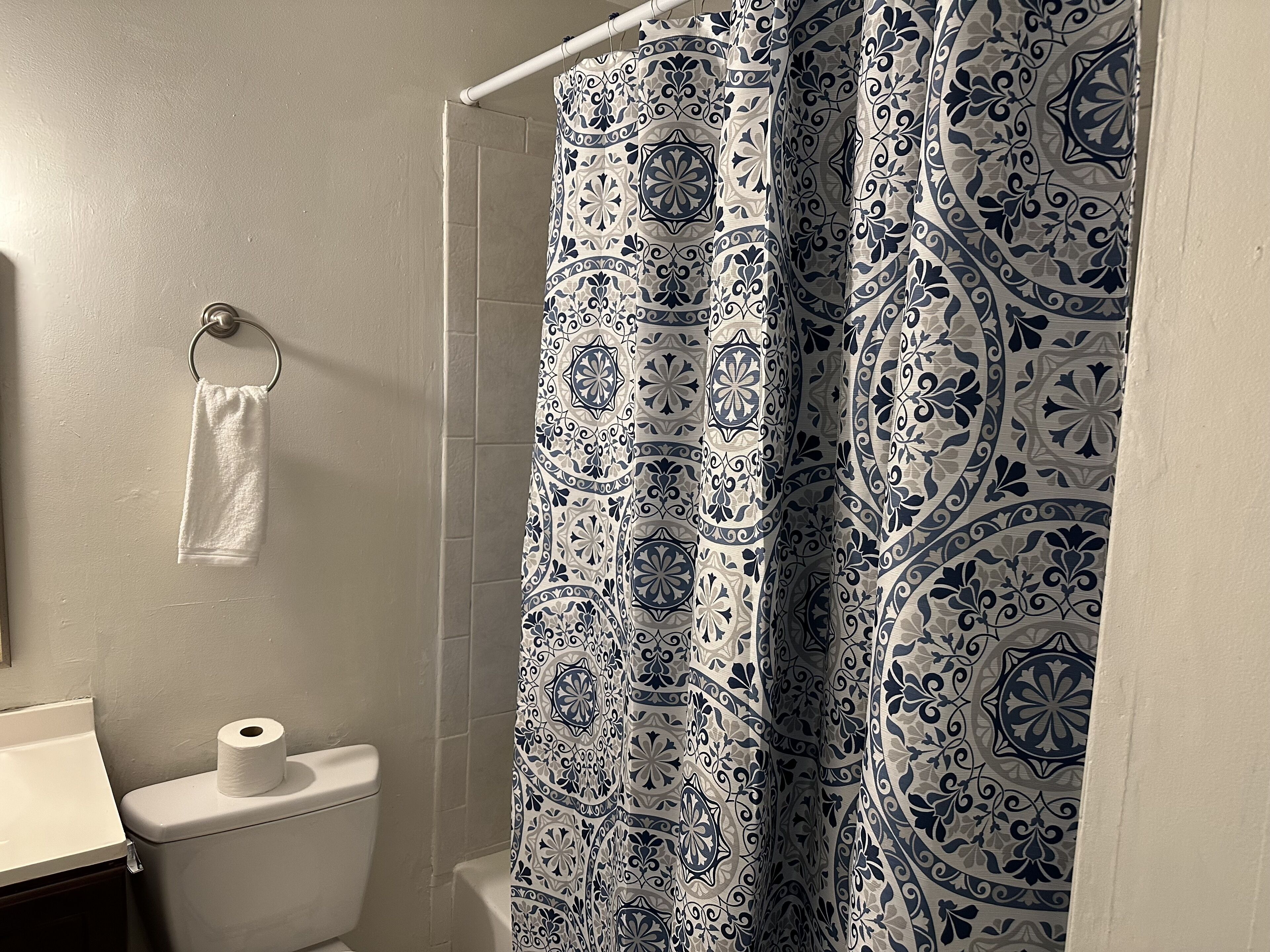 Un baño con cortina de ducha estampada, un inodoro y una toalla colgada en un aro de metal.