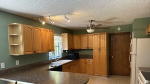 A kitchen with wooden cabinets, a granite countertop, a ceiling fan, and a refrigerator. - Gemme au paradis (Lake Worth)