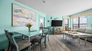 Une pièce aux murs de couleur turquoise, avec une table à manger, des chaises, un canapé et un téléviseur.