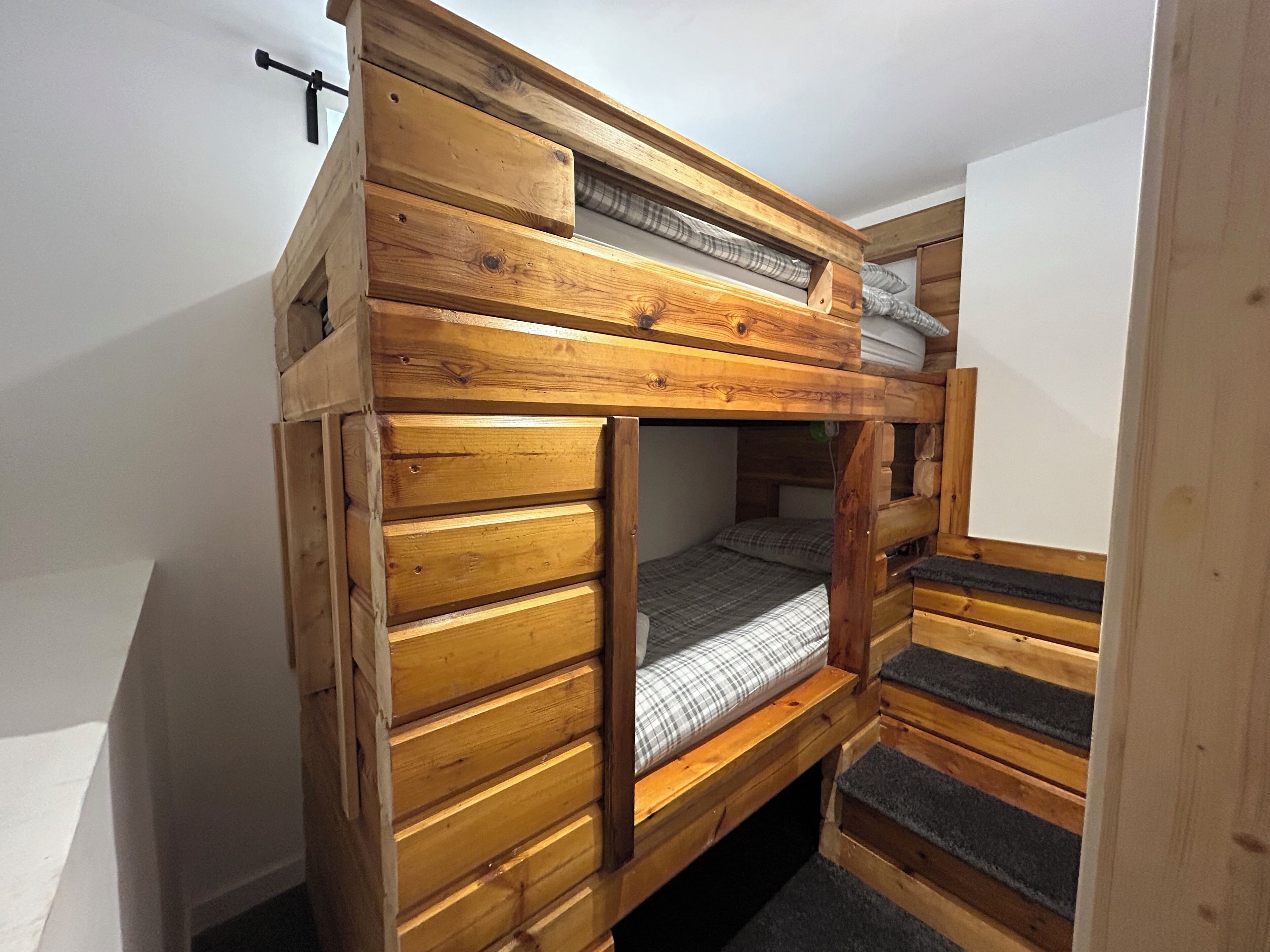 Una cama litera con estructura de madera y colchón con cubierta escocesa.