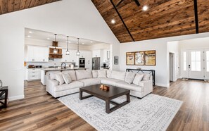 A spacious living area with a large sectional sofa, a coffee table, and a kitchen in the background.