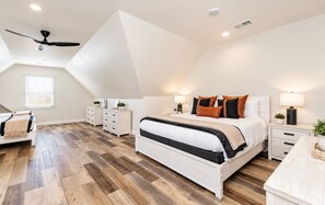 A bedroom with a large bed, a ceiling fan, and a herringbone-patterned wooden floor.