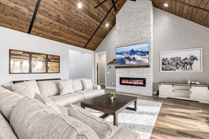 Ein modernes Wohnzimmer mit Kamin aus Stein, einem großen Flachbildfernseher und einer Holzbalkendecke.
