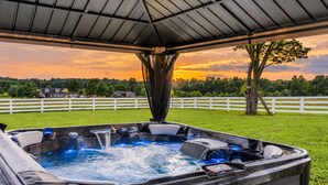 Un jacuzzi bajo una zona techada con vista a una valla blanca y árboles al fondo.