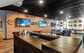 A bar area with a brick wall, wooden bar counter, and seating area with leather chairs.