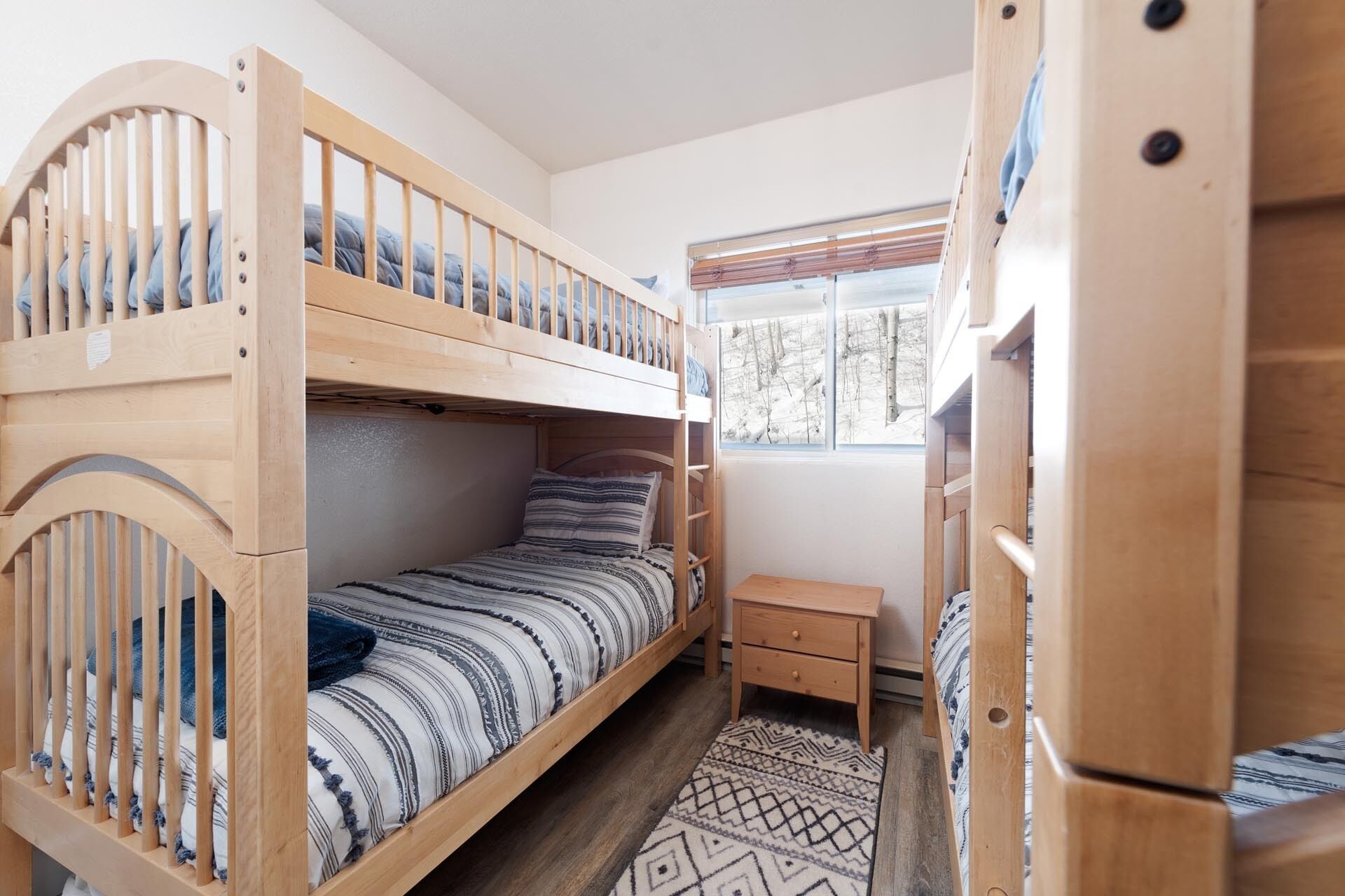 Habitación pequeña con literas, una mesita de noche y ventana con vistas a árboles.