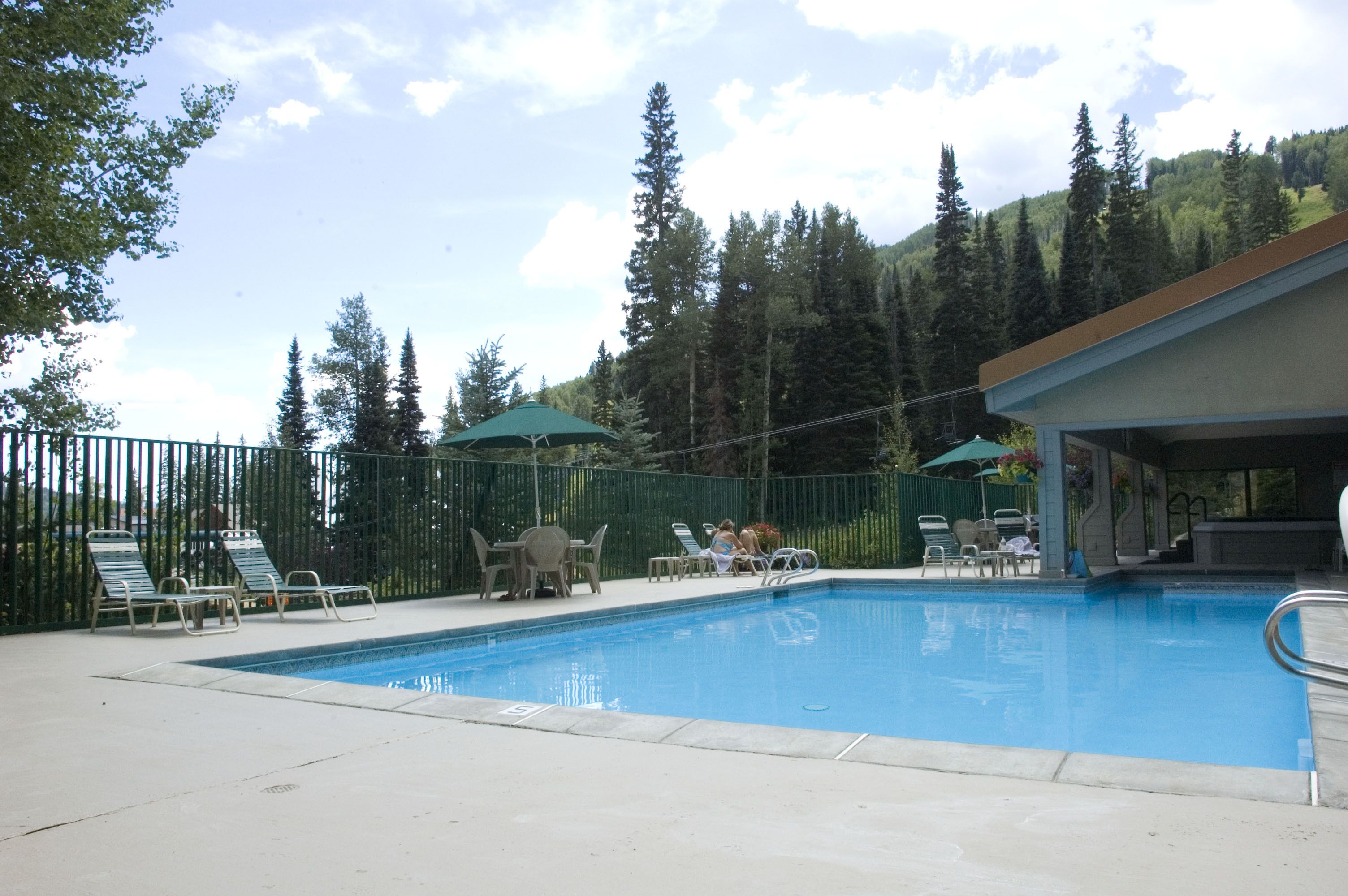 A swimming pool with lounge chairs and umbrellas, surrounded by a fence and trees.