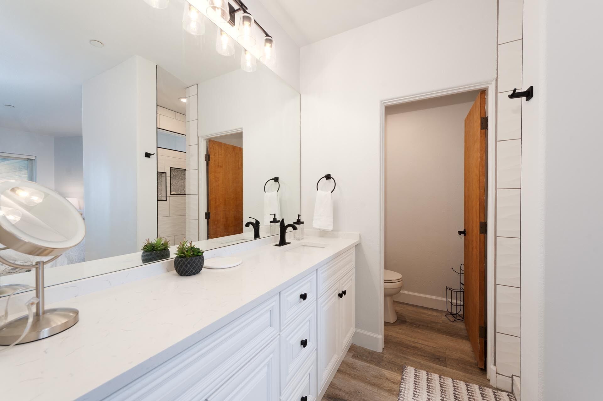 A modern bathroom with a white vanity, a large mirror, and a wooden door leading to another room.
