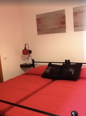 Una cama con ropa de cama roja, un cabecero negro y dos obras de arte colgadas en la pared.