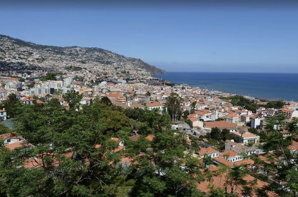 A coastal cityscape with dense residential buildings, a prominent church tower, and a clear view of the sea.