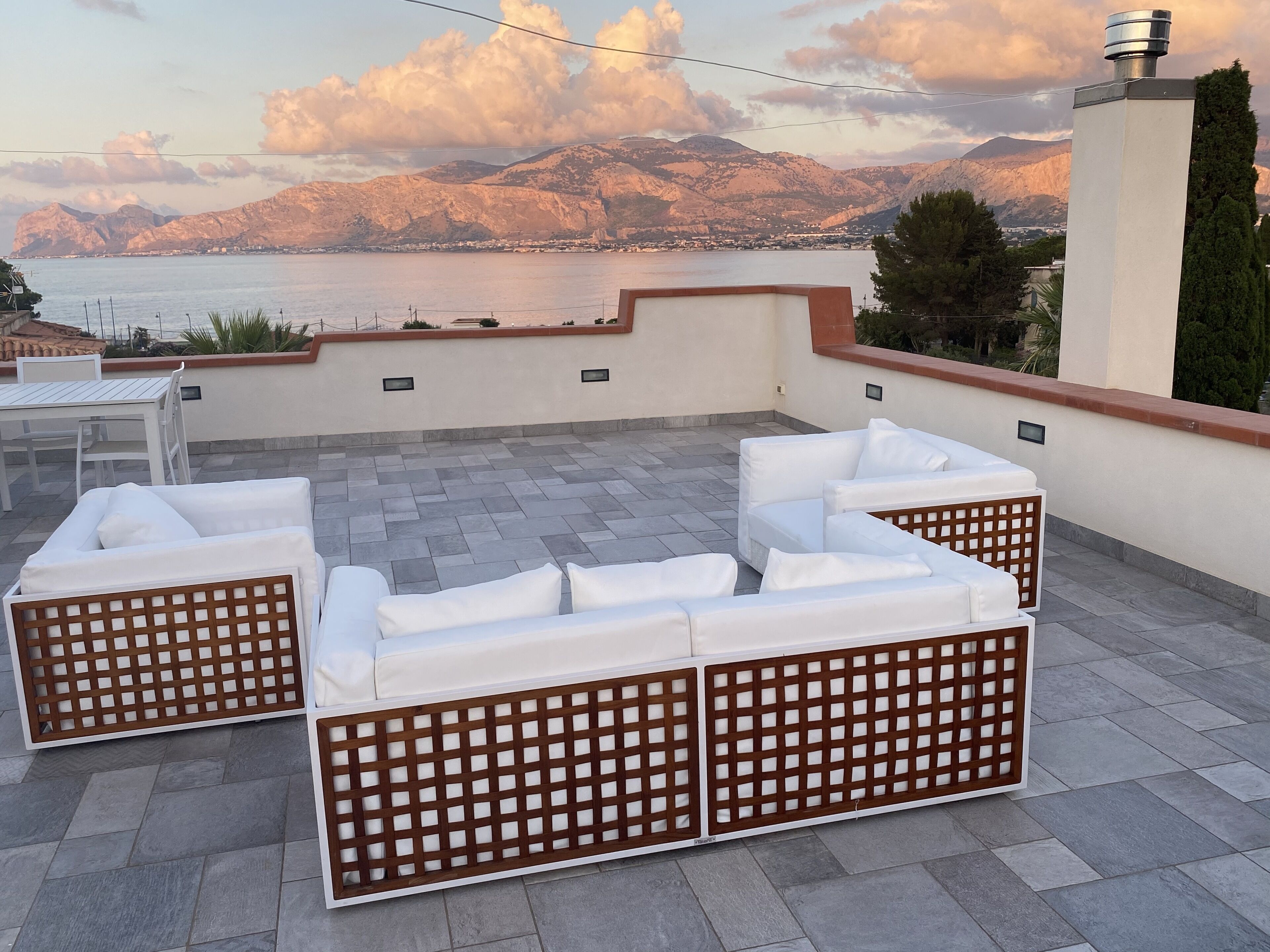 Una terrazza sul tetto con un'area salotto esterna bianca, vista sul mare e montagne sullo sfondo.