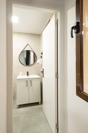 A narrow hallway leading to a bathroom with a white sink, a round mirror, and a white cabinet. - Cosy Room with Bathroom Gran Vía | 034 (Madrid)