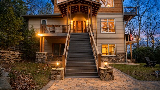 A two-story house with a central staircase, stone walls, and a porch with outdoor lighting. - Luxury Estate & Rustic Mountain Retreat Asheville (Buncombe County)