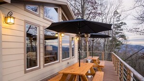 A wooden deck with picnic tables and an umbrella, overlooking a mountainous landscape. - Luxury Estate & Rustic Mountain Retreat Asheville (Buncombe County)