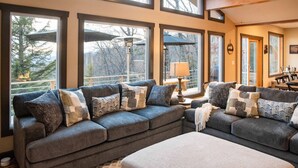 A cozy living room with a large gray sectional sofa, multiple windows offering views of trees and mountains, and a wooden ceiling. - Luxury Estate & Rustic Mountain Retreat Asheville (Buncombe County)
