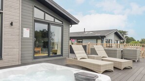 A modern outdoor deck with a hot tub, lounge chairs, and a wooden fence. - Mordros Lodge (Redruth)