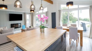 A modern kitchen with a central island, pendant lighting, and a view of the outdoors. - Mordros Lodge (Redruth)