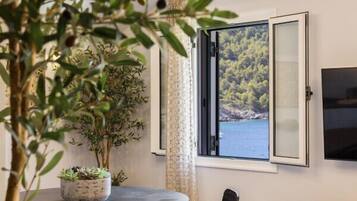 Un coin repas avec une table ronde, deux chaises, une plante en pot et une vue sur un paysage côtier par la fenêtre.