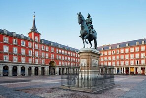 A plaza with a statue of a man on horseback, surrounded by red buildings with multiple windows and a church spire in the background.