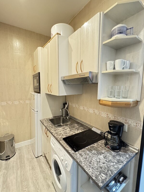 A compact kitchen with a washing machine, microwave, and coffee maker.