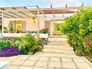 A covered outdoor area with steps leading to a house entrance, surrounded by lush greenery and a stone wall. - CASA BADANA Exclusive House with amazing views. (CN)