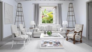 Una sala de estar moderna con un sofá blanco, dos sillones, una mesa de centro con revistas y vistas a la vegetación a través de un amplio ventanal.