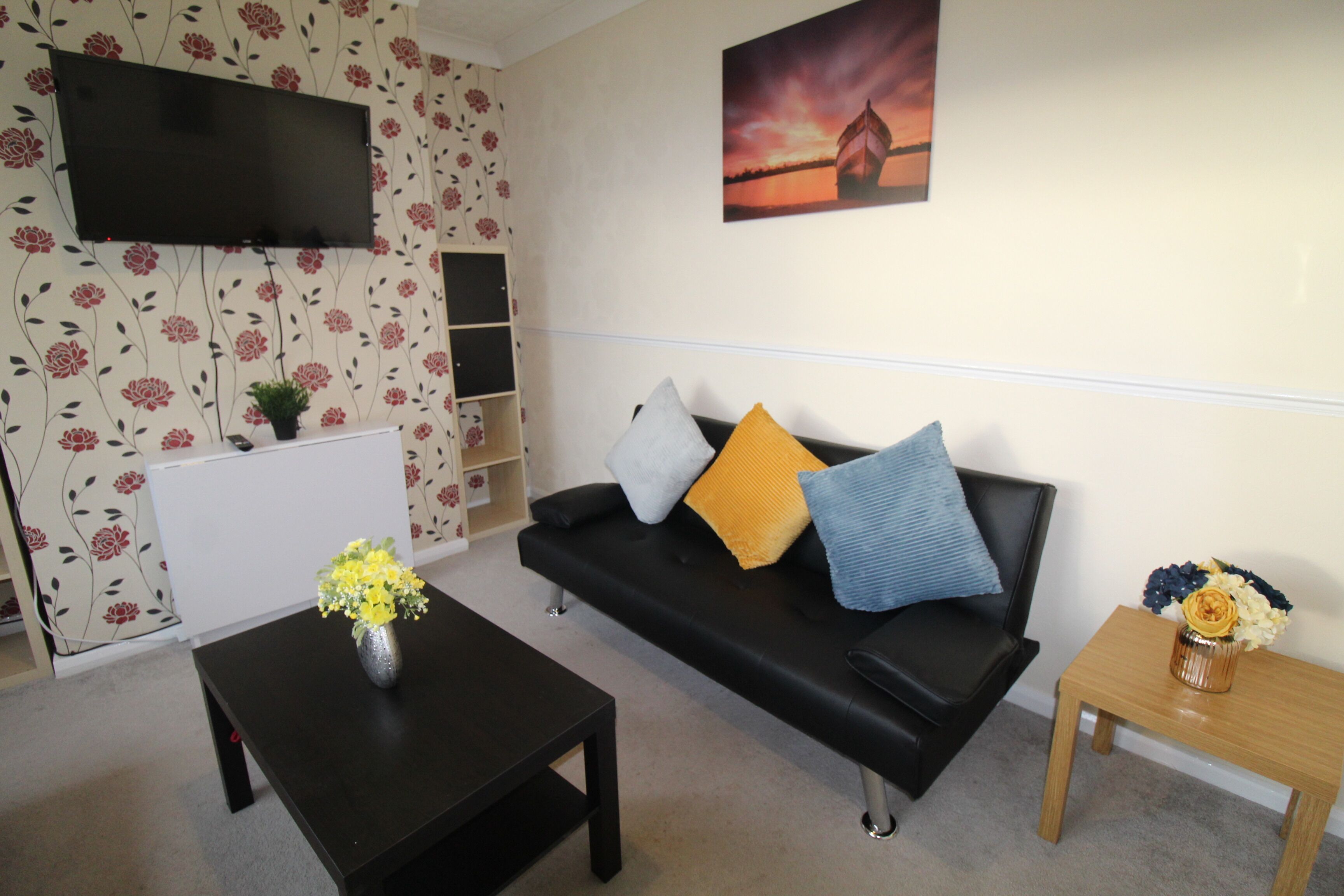 A living room with a black sofa, a coffee table, a TV mounted on the wall, and a painting above the sofa.