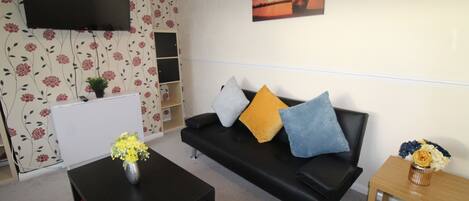 A living room with a black sofa, a coffee table, a TV mounted on the wall, and a painting above the sofa.