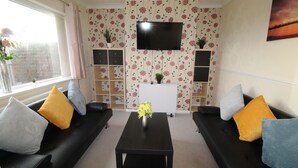 A living room with two black sofas, a coffee table, and a TV mounted on the wall. - Pavement House (Sutton-in-Ashfield)