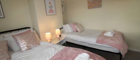 A hotel room with two beds, each with pink and white bedding, a nightstand with a lamp, and artwork on the walls.