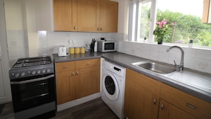 A kitchen with wooden cabinets, a stove, a washing machine, a microwave, and a sink. - Pavement House (Sutton-in-Ashfield)