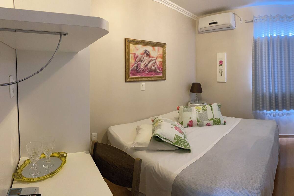A hotel room with a bed, a bedside table with a lamp, a painting on the wall, and a TV mounted on the wall.