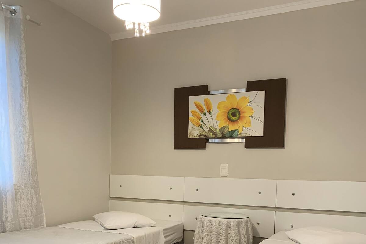 A hotel room with two beds, a ceiling light, a wall-mounted painting, and a wooden floor.