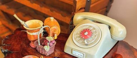 Un teléfono antiguo, una estantería de madera para vinos y una mesa rústica con una vela y un pequeño cuenco.